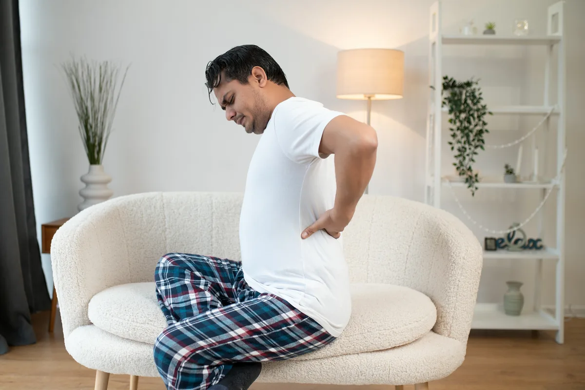 Man seated on a sofa holding his lower back in pain